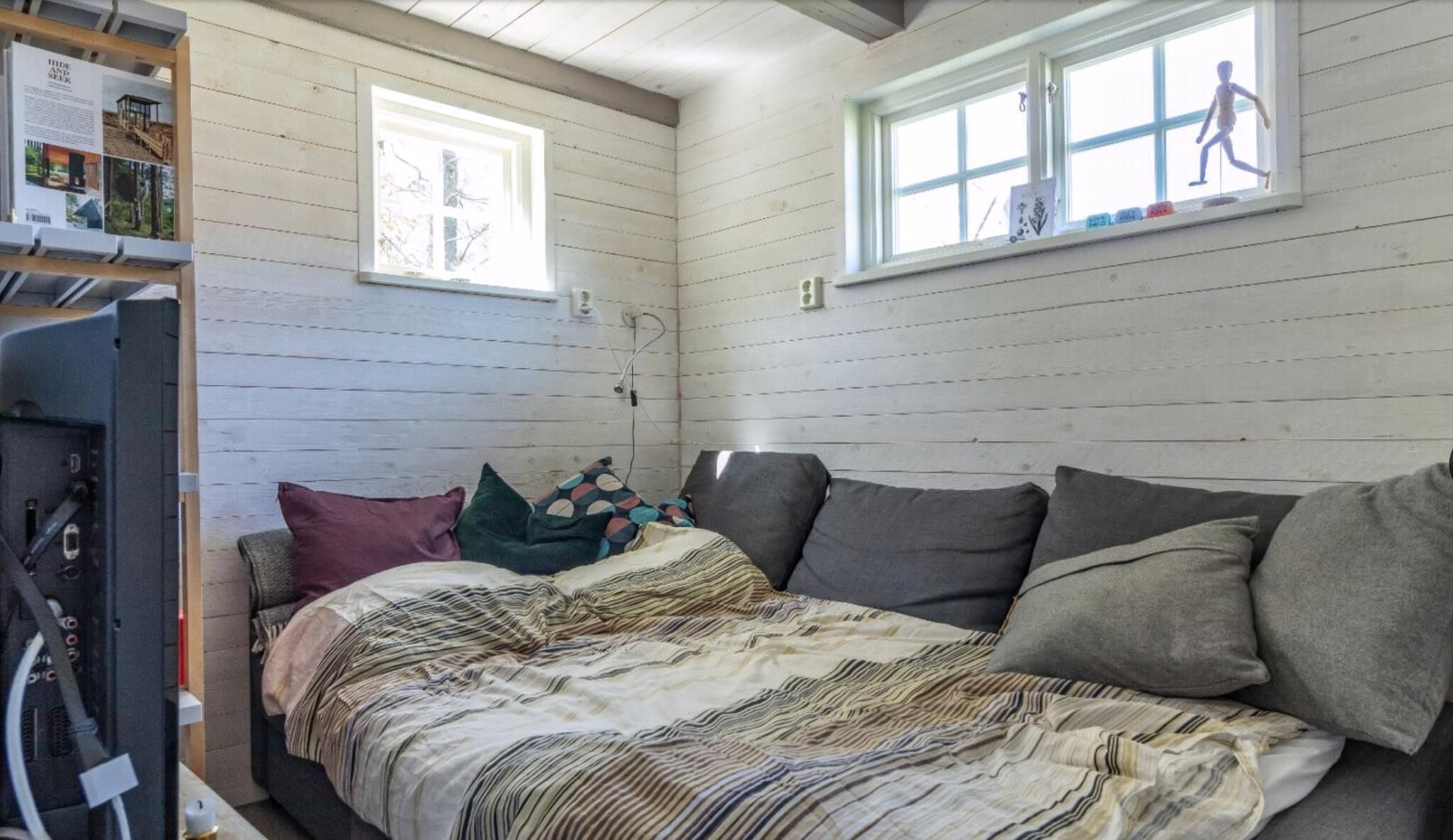 A bedroom with a bed, pillows, a window, and a wall-mounted shelf with items.