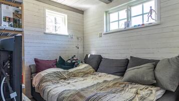 A bedroom with a bed, pillows, a window, and a wall-mounted shelf with items.