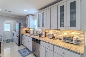 A modern kitchen with white cabinetry, a granite countertop, a dishwasher, a coffee maker, and a toaster oven. - Energy Corridor 4BR | Near I-10 & Hwy 6 (Houston)