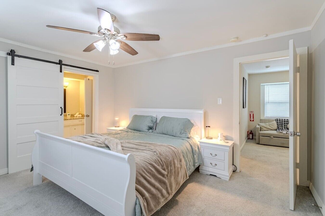 A bedroom with a bed, nightstands, a ceiling fan, and a door leading to another room.
