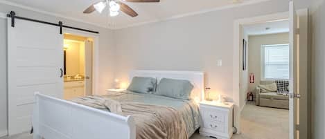 A bedroom with a bed, nightstands, a ceiling fan, and a door leading to another room.