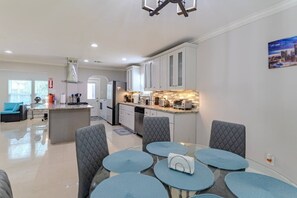 A modern kitchen with white cabinets, a central island, and a dining area with a round table and grey upholstered chairs. - Energy Corridor 4BR | Near I-10 & Hwy 6 (Houston)