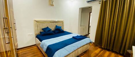 A hotel room with a bed, wooden flooring, a ceiling fan, and a window with curtains.