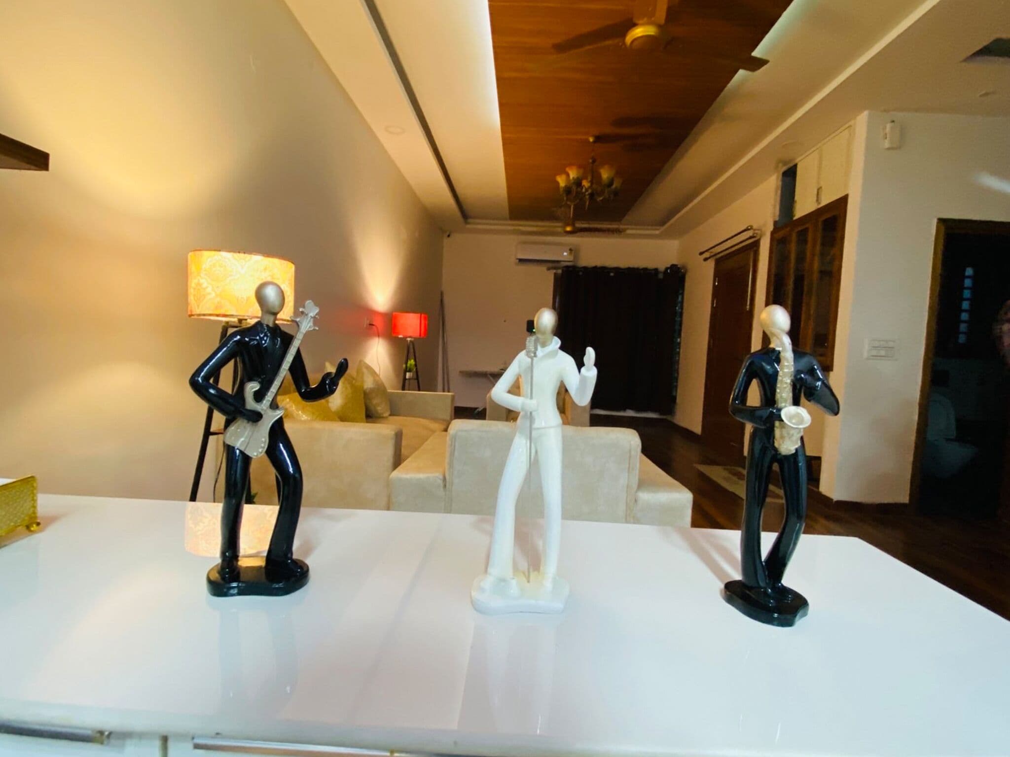 Una habitación con una mesa blanca que muestra tres figuritas, una lámpara y un sofá.