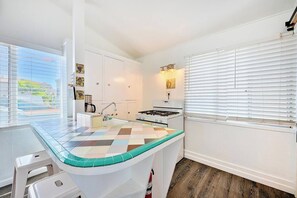 A compact kitchen with a central island, a stove, and a sink. - Beach Break by Coastline Vacation Rentals (San Diego)