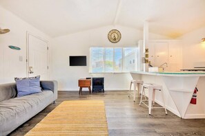 A modern living room with a sofa, a fireplace, a kitchen area with stools, and a large window. - Beach Break by Coastline Vacation Rentals (San Diego)