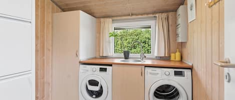 A compact laundry room with two washing machines, a sink, and a window with curtains.
