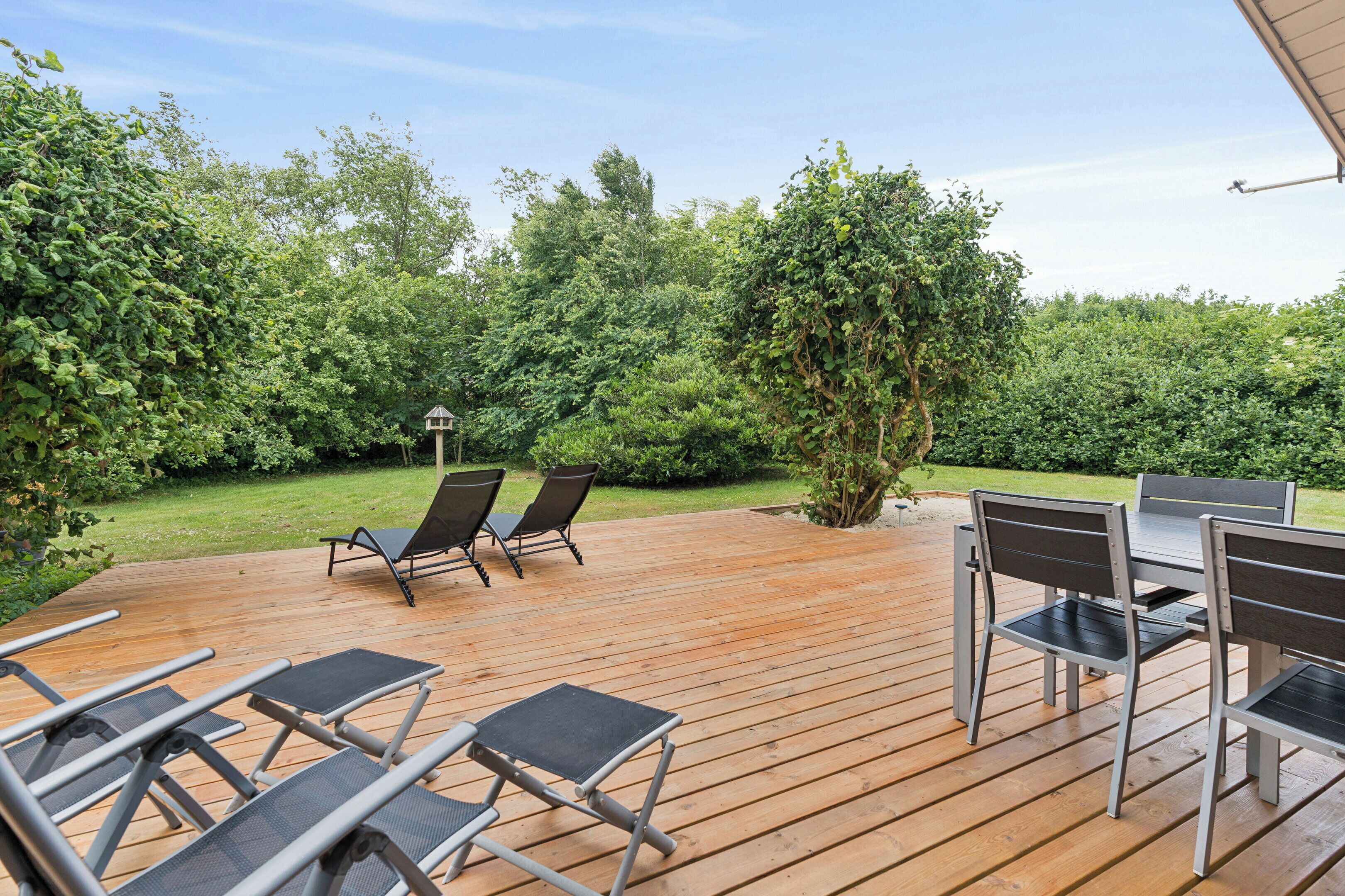 An outdoor deck with a table and chairs, surrounded by lush greenery.