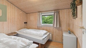 Ett rum med träväggar, en säng, ett fönster med gardiner, en vägglampa och ett litet bord med en vas.