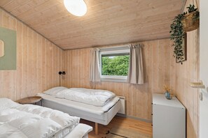 Ein Zimmer mit Holzwänden, einem Bett, einem Vorhangfenster, einer Wandleuchte und einem kleinen Tisch mit einer Vase.