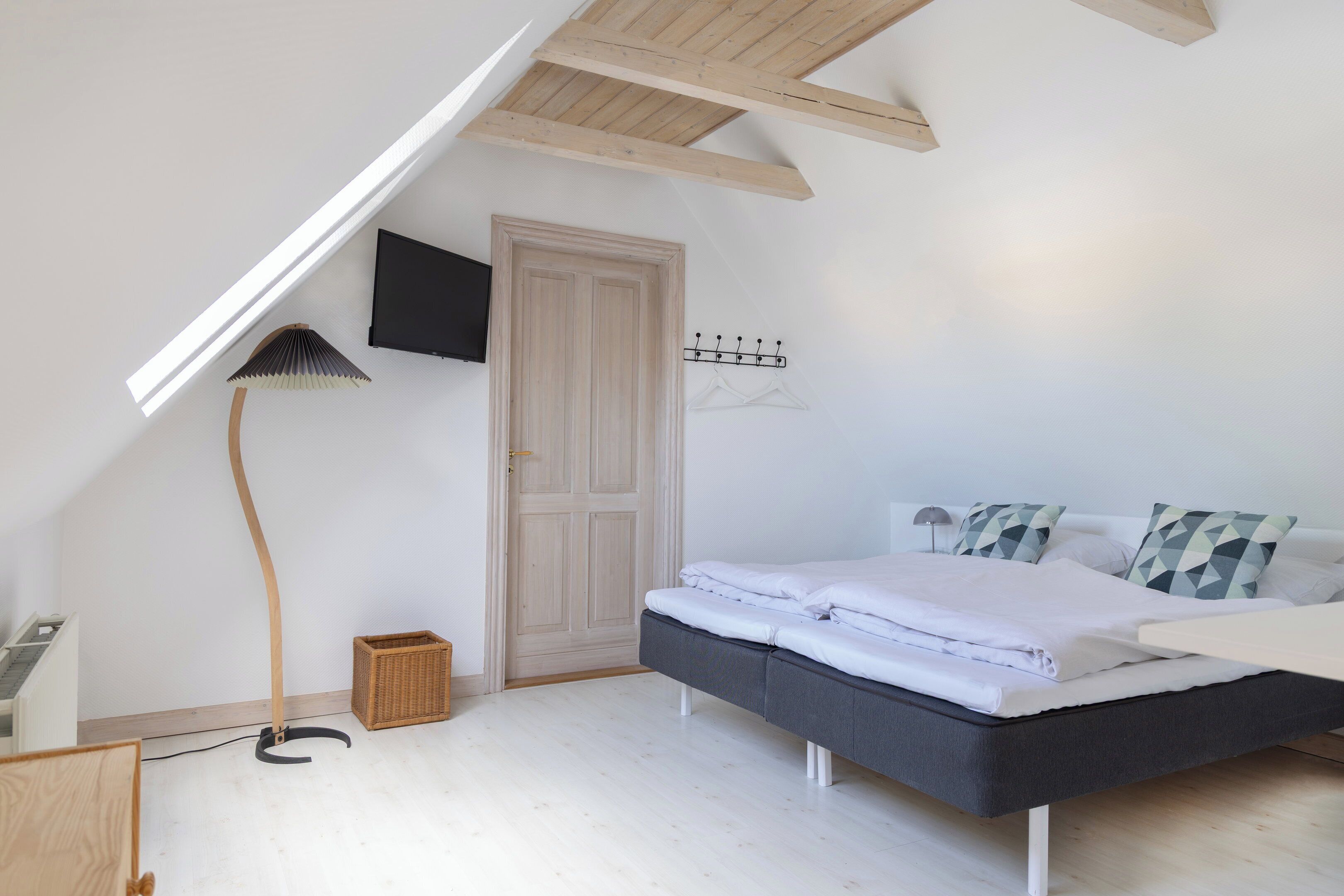 A bedroom with a sloped ceiling, a bed, a television, a coat rack, and a floor lamp.