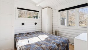 Een slaapkamer met een bed, twee ramen, een radiator en een witte dressoir.