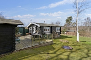 A wooden cabin with a deck, a small table, and a chair. - Authentic holiday home with Baltic Sea view (Allinge-Sandvig)