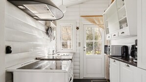 Een kleine keuken met witte kastjes, een magnetron, een koffiezetapparaat en een raam met uitzicht op bomen.