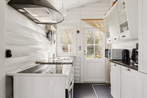A compact kitchen with white cabinetry, a microwave, a coffee maker, and a window with a view of trees. - Authentic holiday home with Baltic Sea view (Allinge-Sandvig)