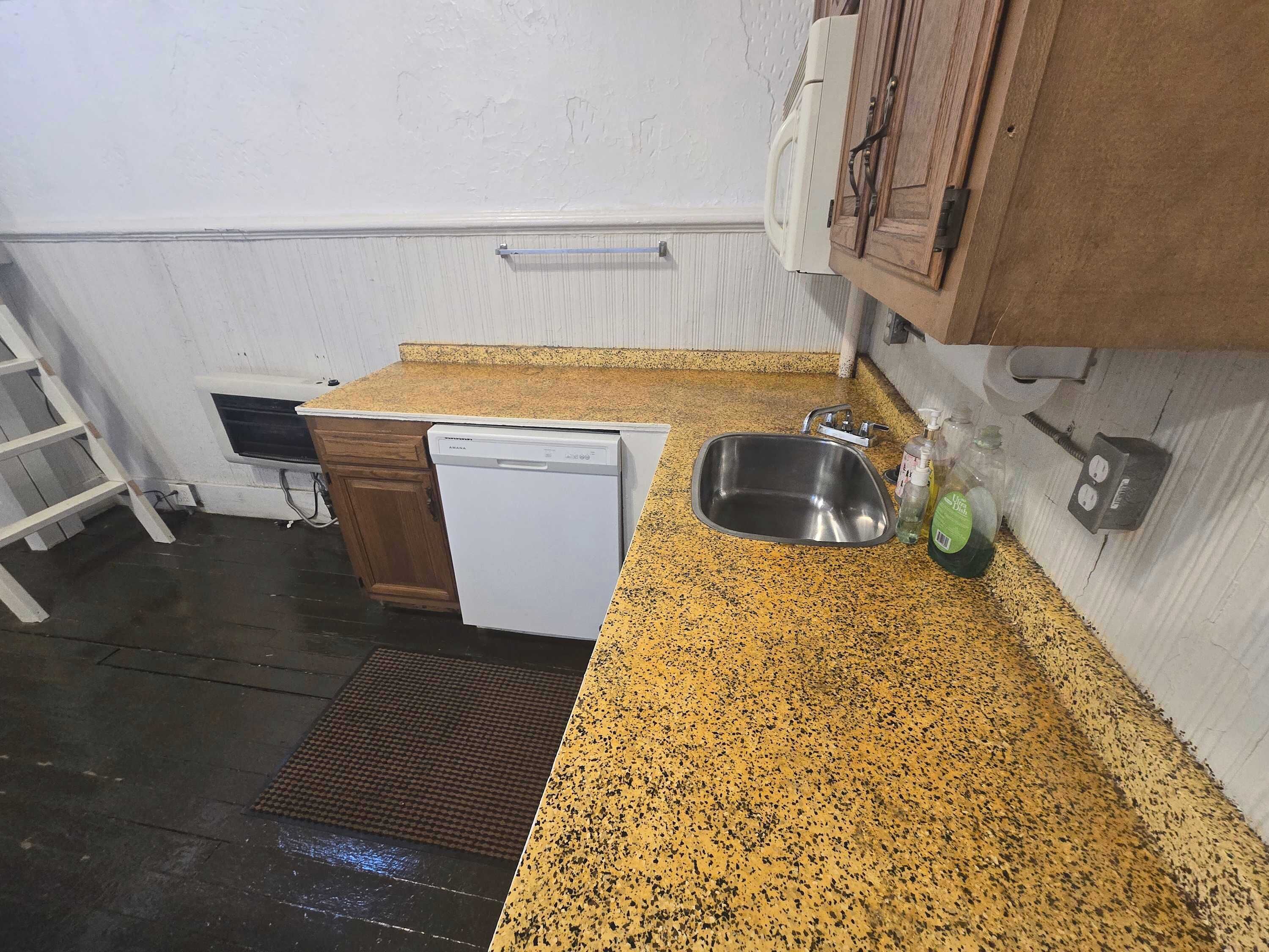 Cozinha compacta com máquina de lavar louça, pia de aço inoxidável e bancada de granito.