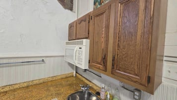 A kitchen with a granite countertop, a stainless steel sink, wooden cabinets, a microwave, and a painting on the wall.