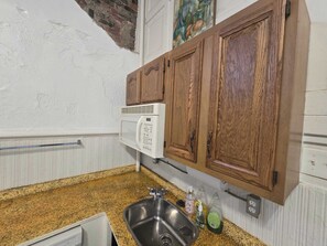 Eine Küche mit einer Granit-Arbeitsplatte, einem Edelstahl-Spülbecken, Holzschränken, einer Mikrowelle und einem Bild an der Wand.