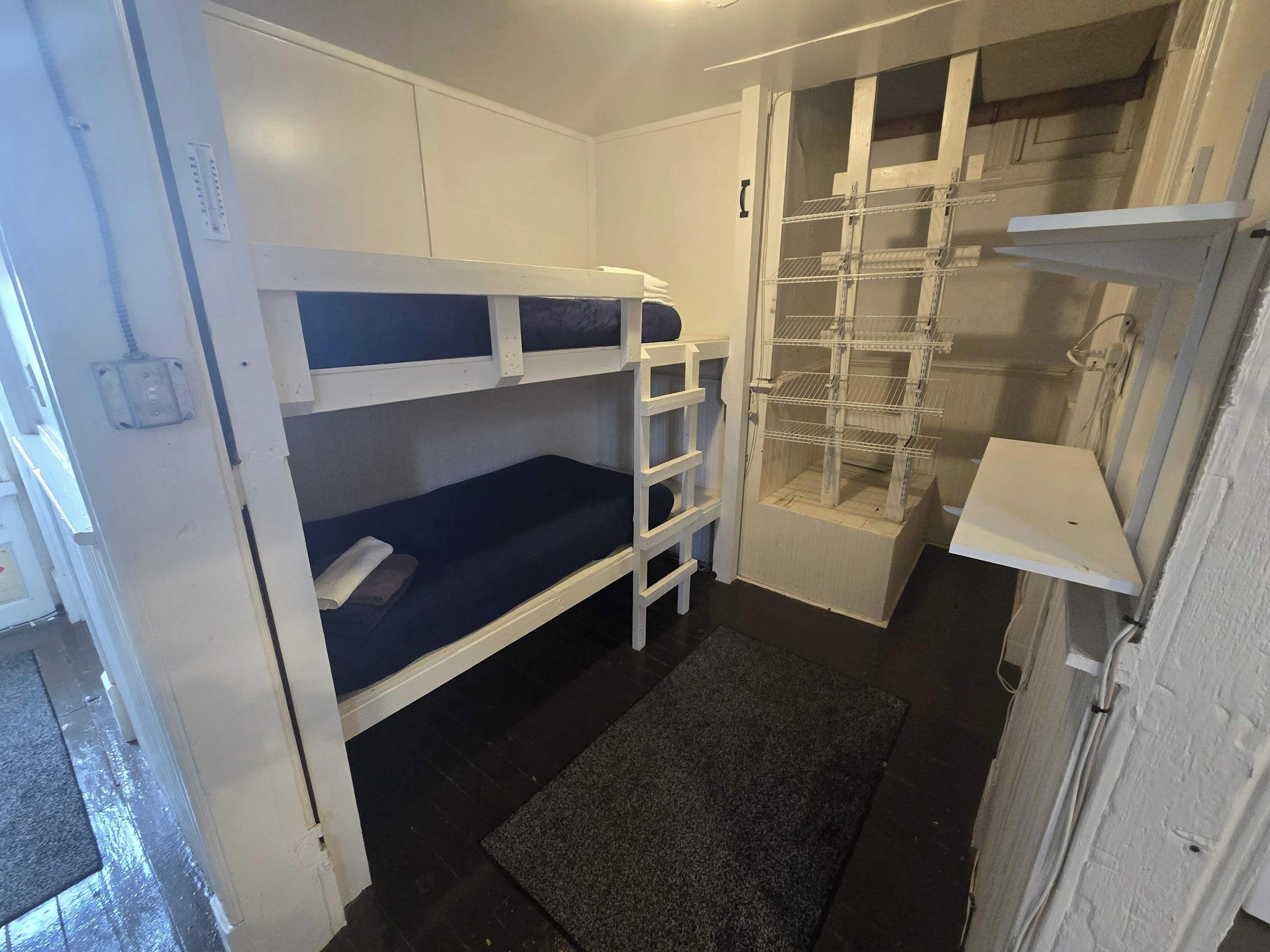A compact room with bunk beds, a small shelf unit, and a door leading to a storage area.