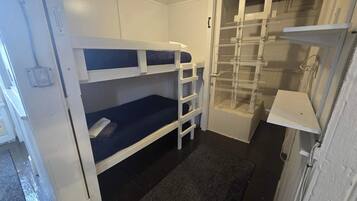 Une petite pièce avec des lits superposés, une petite étagère et une porte donnant sur un espace de rangement.