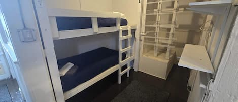 A compact room with bunk beds, a small shelf unit, and a door leading to a storage area.