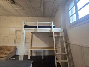 Ein Stockbett mit einer Stehle, ein kleiner Tisch und ein Sofa in einem Zimmer mit weißen Wänden und einem Fenster.