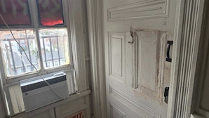 A white door with a traditional design, an exit sign, and a window with a view of buildings outside.