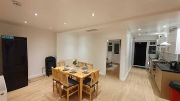 A modern kitchen with a dining area, wooden table, chairs, and a refrigerator.