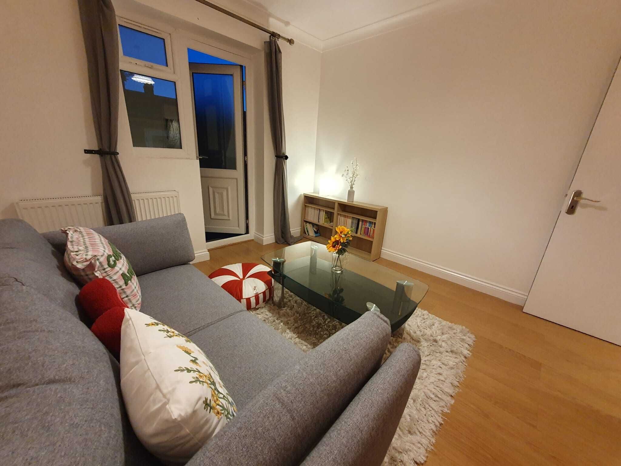 A living room with a grey sofa, a glass coffee table, a bookshelf, and a door.