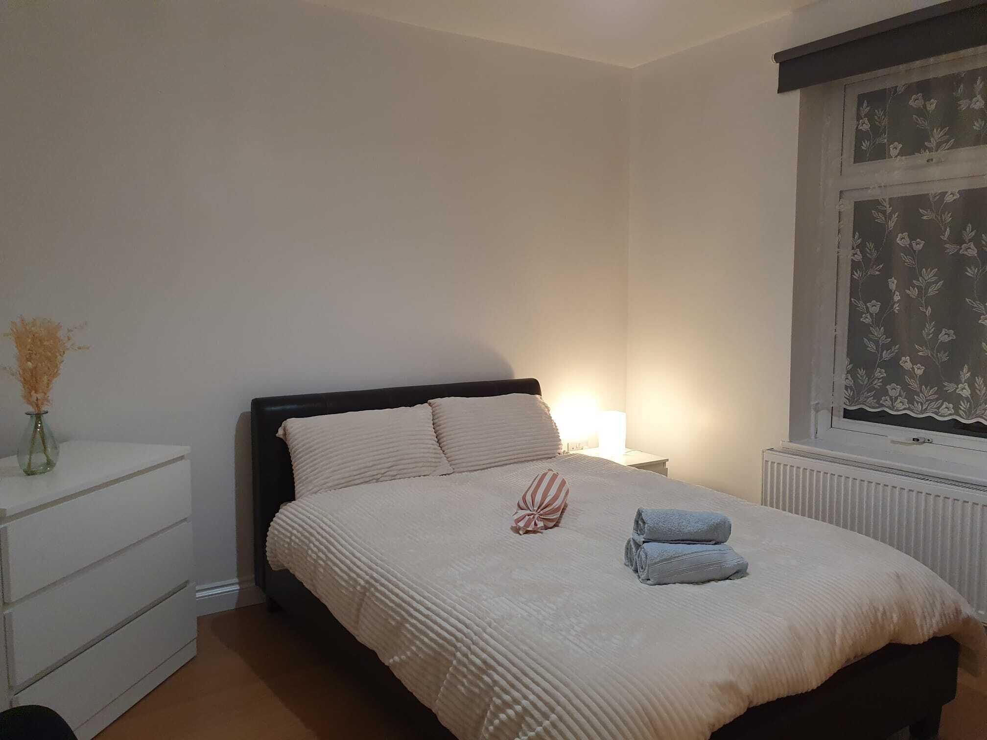 A bedroom with a bed, bedside table, lamp, and a window with floral curtains.