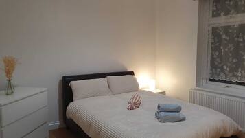A bedroom with a bed, bedside table, lamp, and a window with floral curtains.