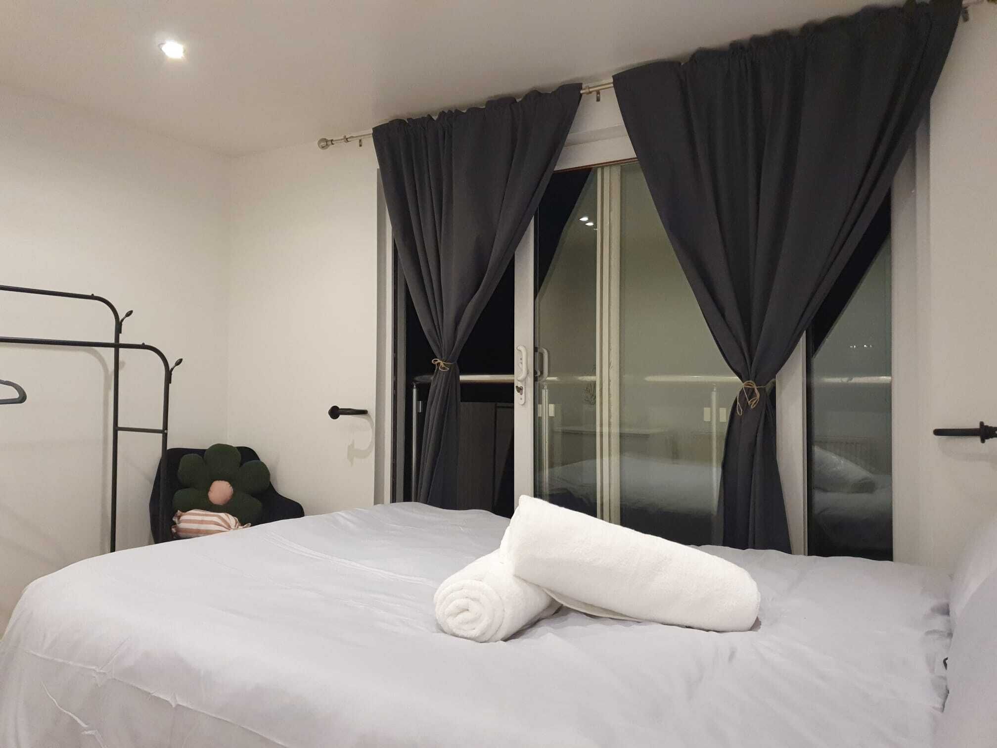 Hotellihuone, jossa on sänky, ikkuna verhoilla, metallinen sängynrunko ja tyyny.