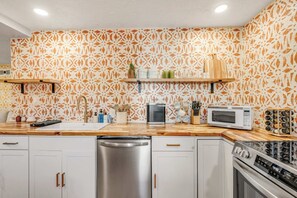 Una cocina con gabinetes blancos, electrodomésticos de acero inoxidable y papel tapiz estampado.