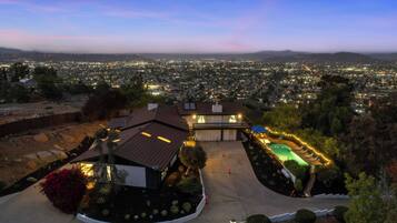 A residential property with a swimming pool, a covered patio, and a view of a cityscape at dusk.
