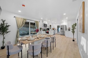 A modern kitchen with white cabinets, stainless steel appliances, and a dining area with a wooden table and chairs. - Pool, Big Yard, View, King Bed, Parking, 4BR - 2.5Bth (El Cajon)