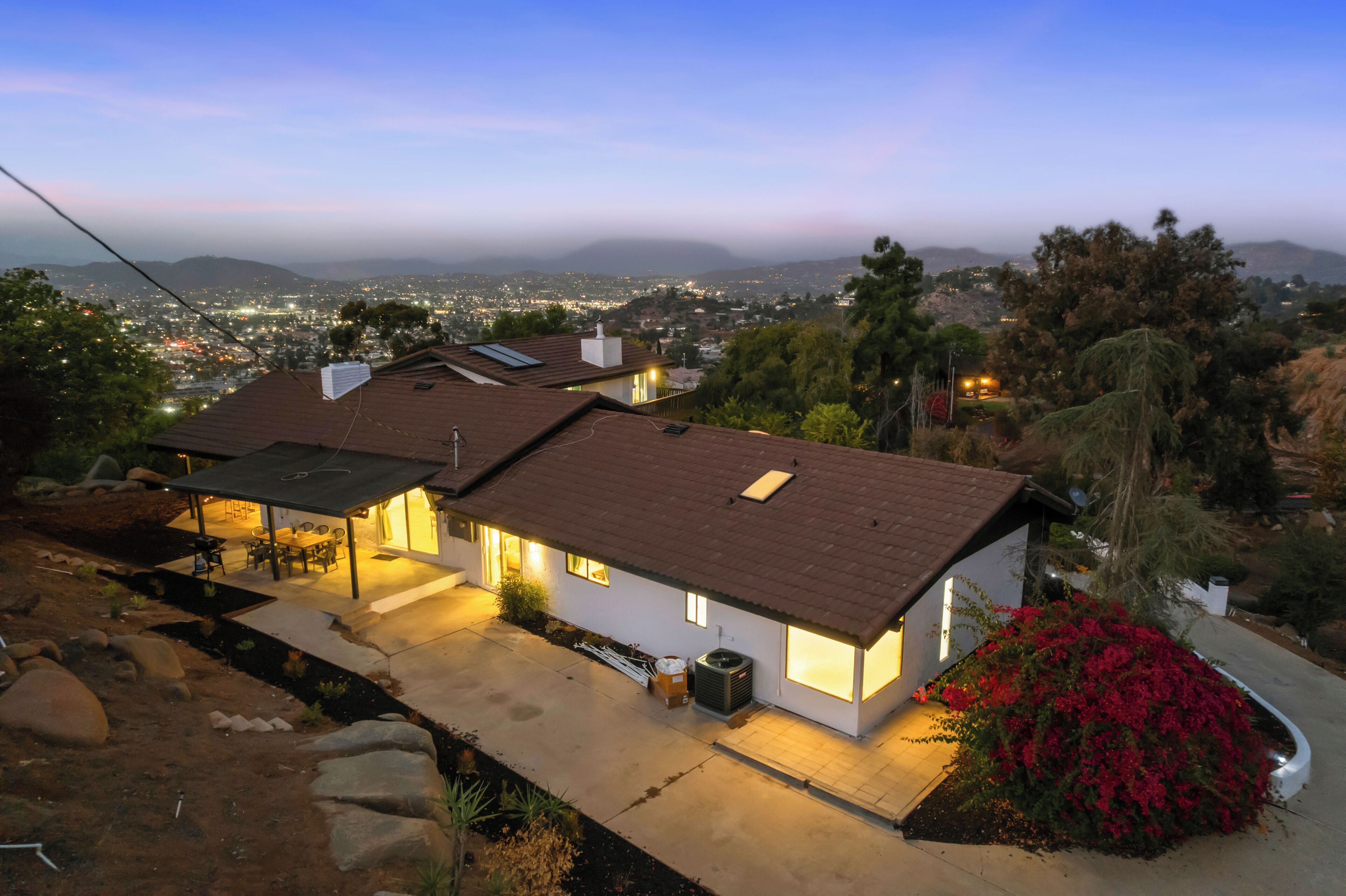 A modern house with a sloped roof, a covered patio, and a view of a cityscape in the background.