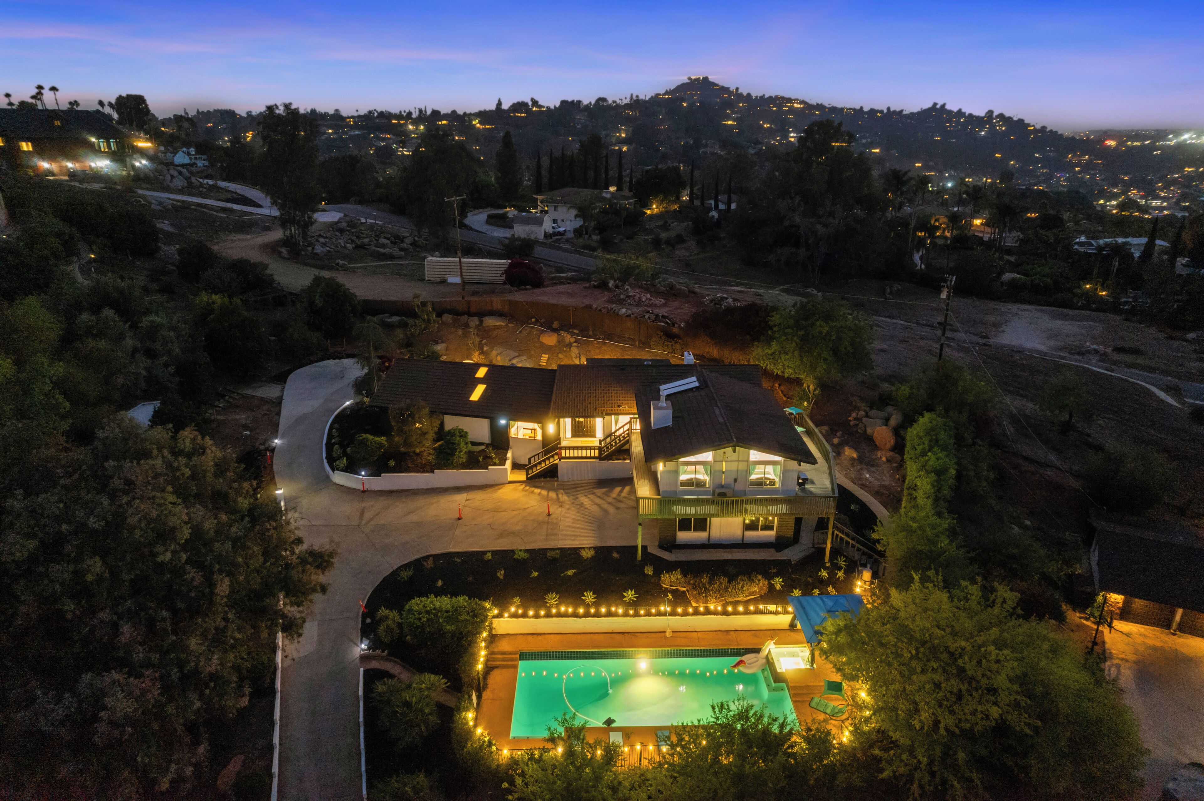 A large house with a swimming pool, surrounded by trees and a hilly landscape.