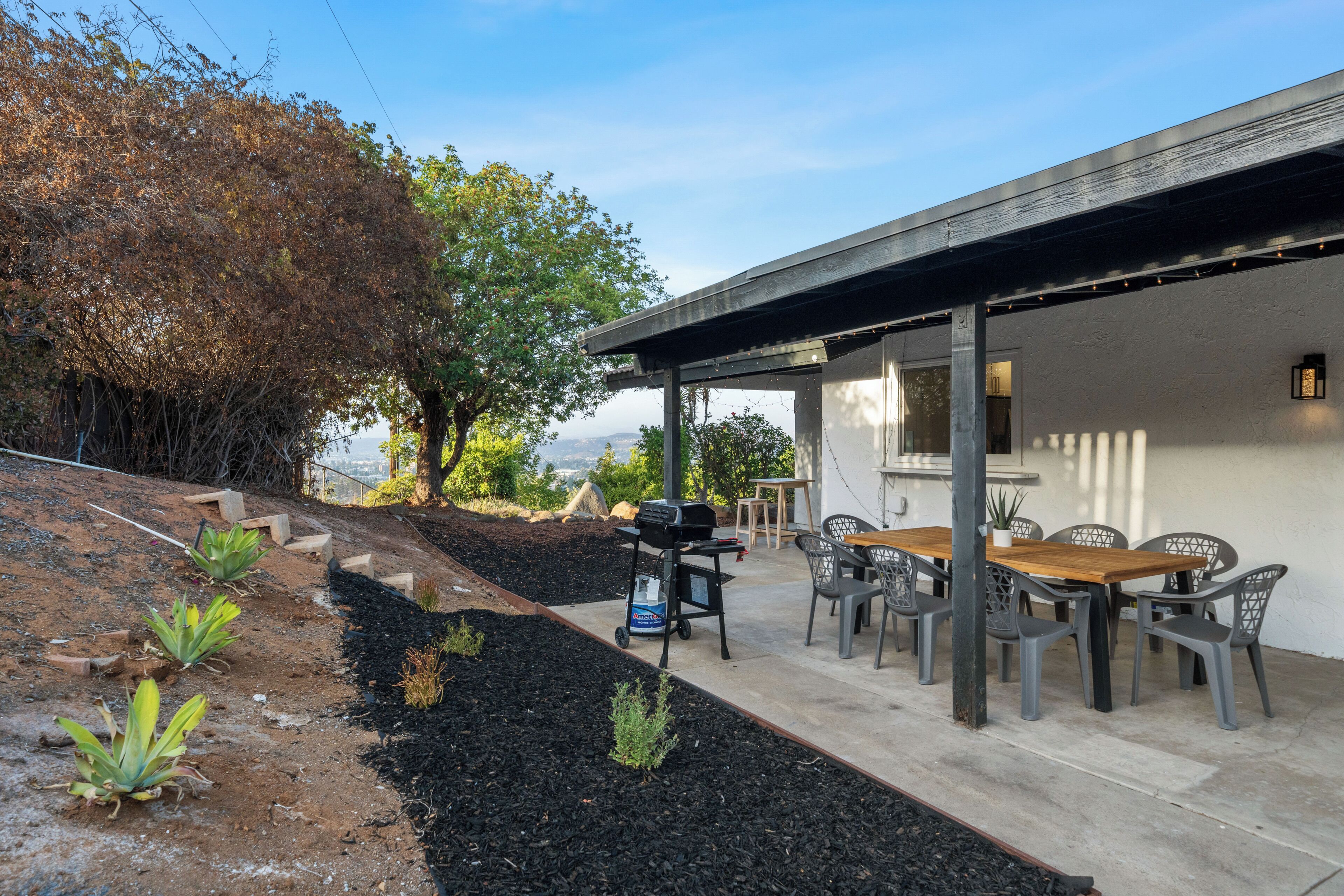 A patio with a dining table and chairs, a grill, and a view of the landscape.