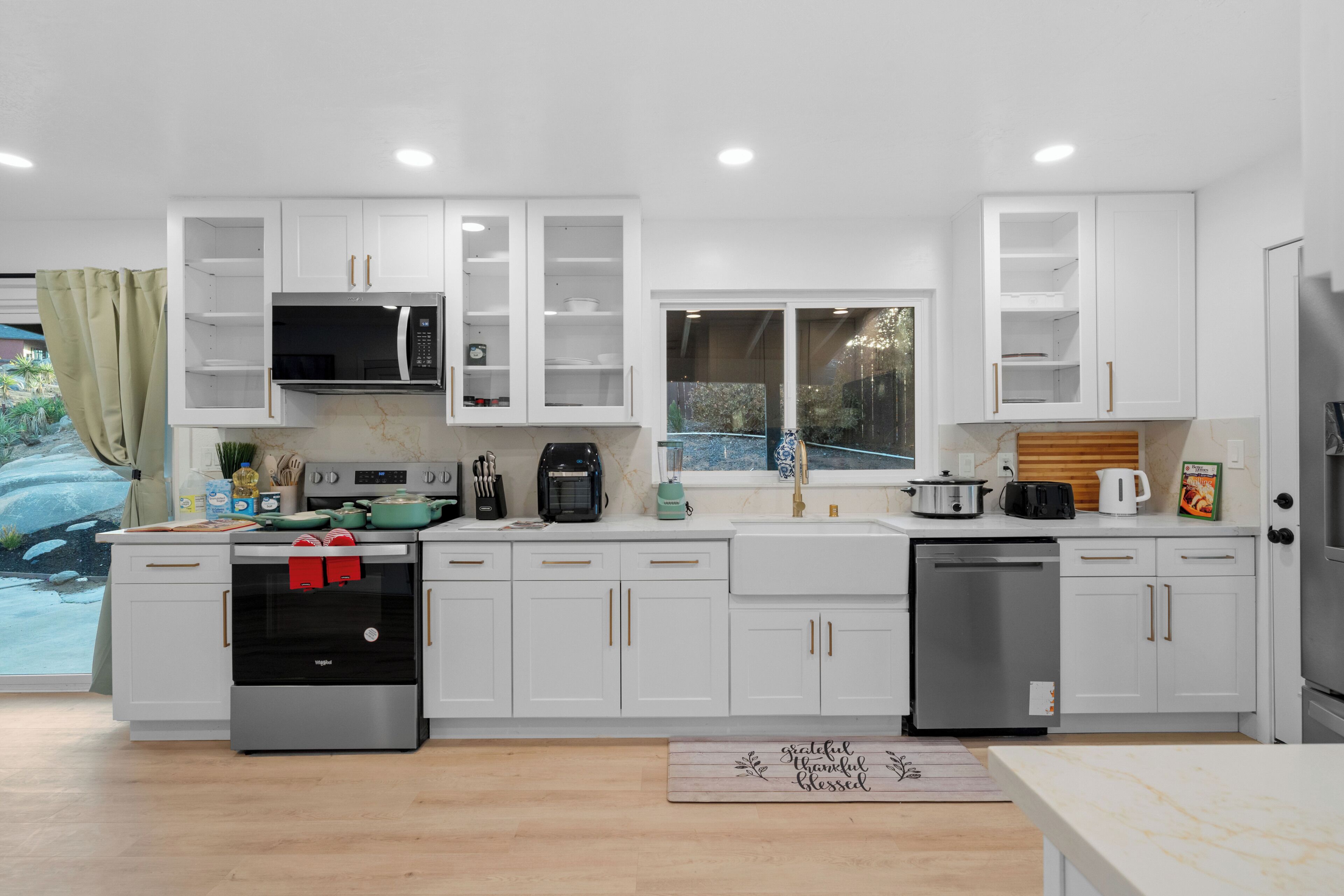 A modern kitchen with white cabinets, stainless steel appliances, and a window overlooking a garden.