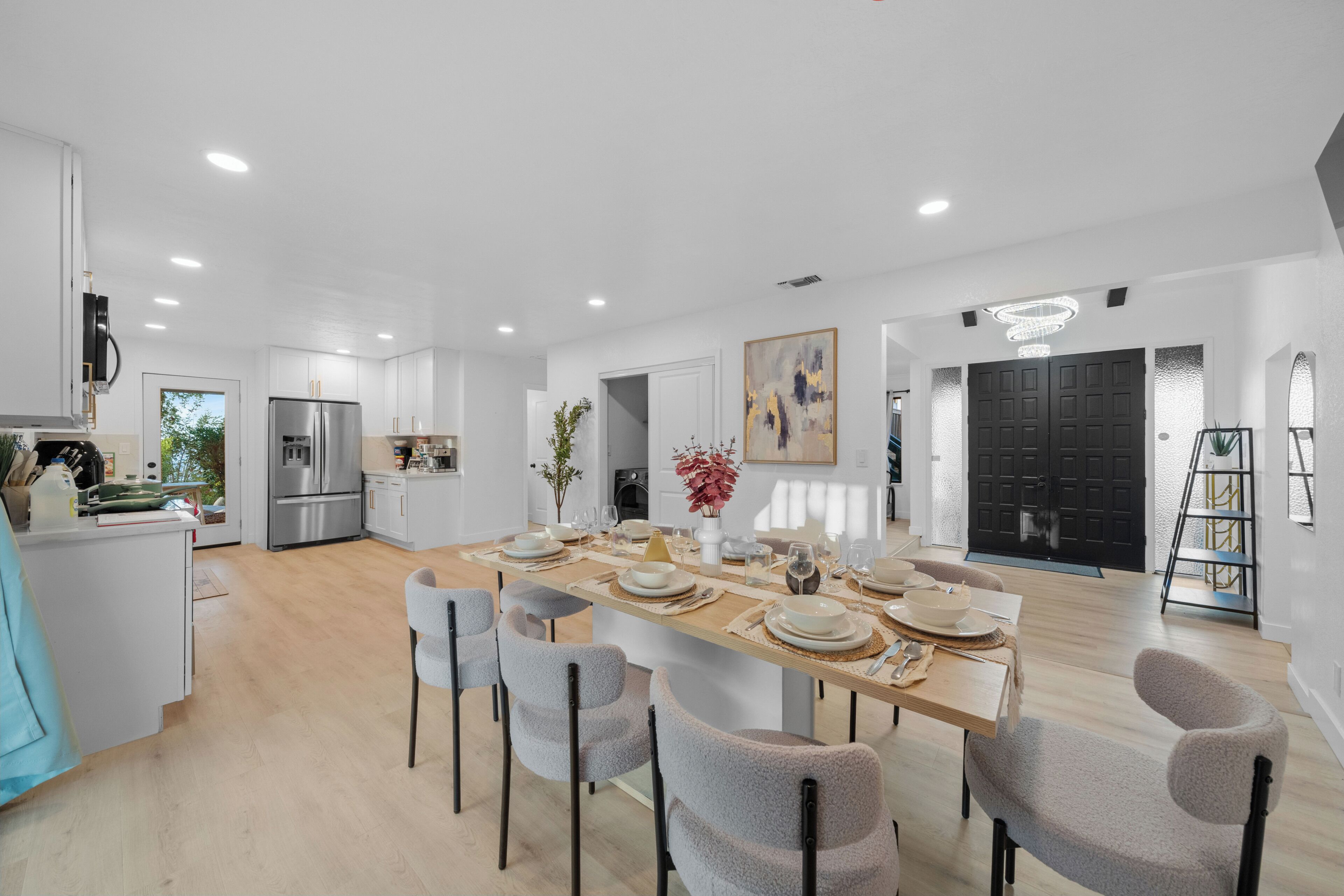 A spacious kitchen with modern appliances, a dining area with a wooden table set for six, and a large black door.
