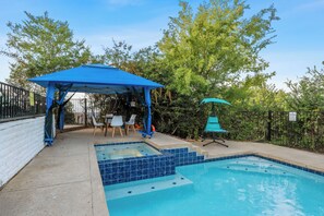 Une piscine dont le bord est recouvert de carreaux bleus, un espace de détente couvert avec des chaises, et un kiosque.