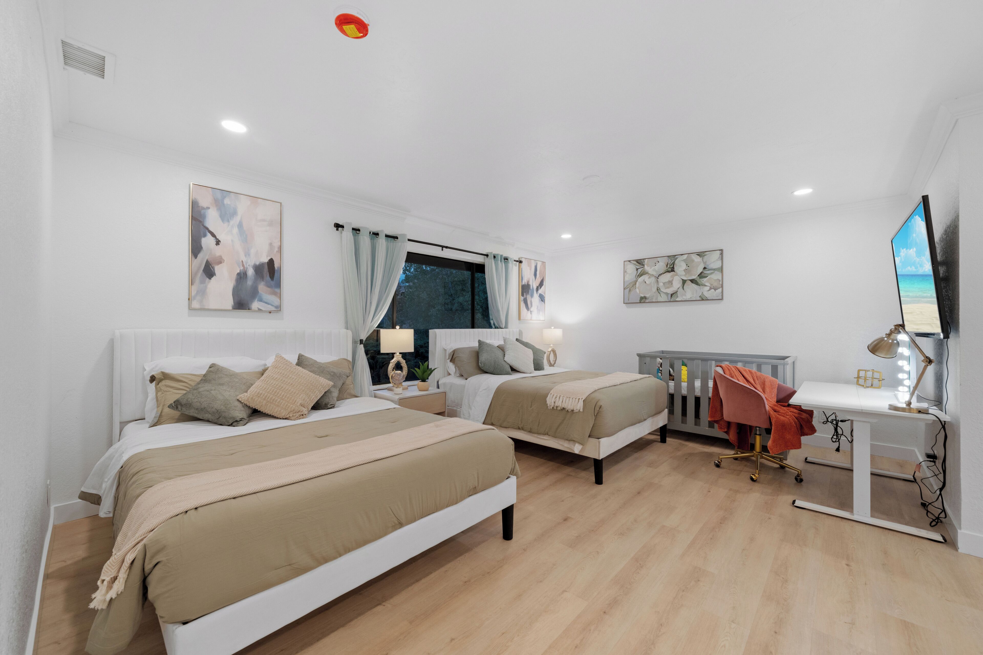 A bedroom with two beds, a desk, a chair, and a TV.