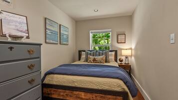 A bedroom with a bed, dresser, and a window with a view of greenery.