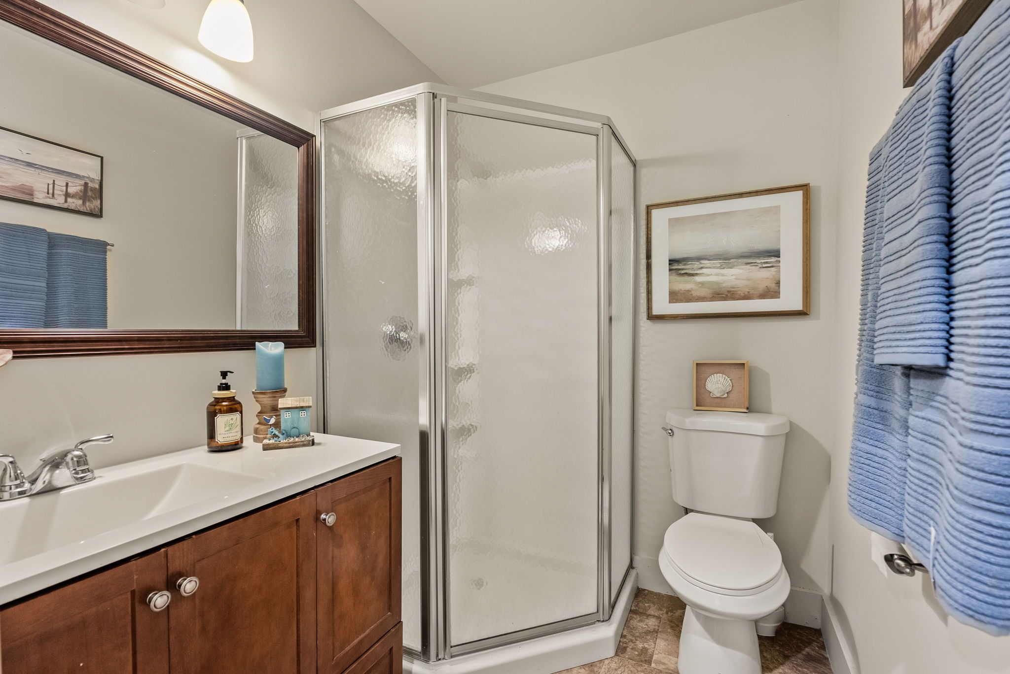 A bathroom with a glass shower enclosure, a white toilet, and a vanity with a mirror.