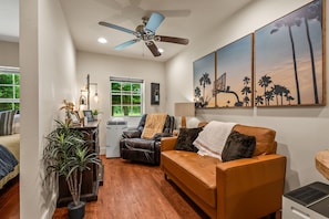 A living room with a ceiling fan, a sofa, a chair, a table with a lamp, and a window with a view of trees.