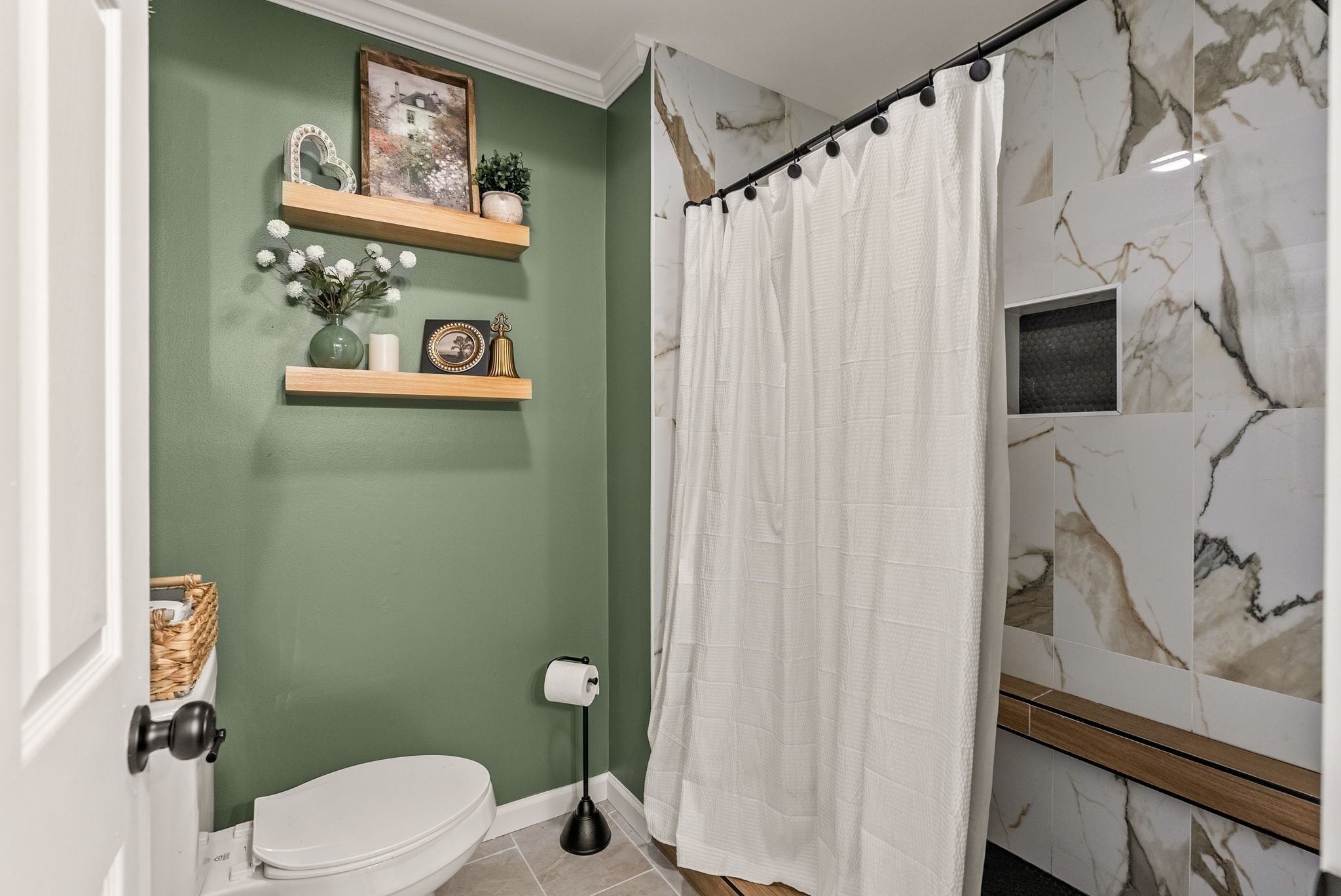 Een badkamer met toilet, douchegordijn, marmeren tegels en een plank met decoratieve objecten.