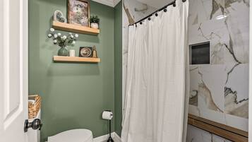 Een badkamer met toilet, douchegordijn, marmeren tegels en een plank met decoratieve objecten.