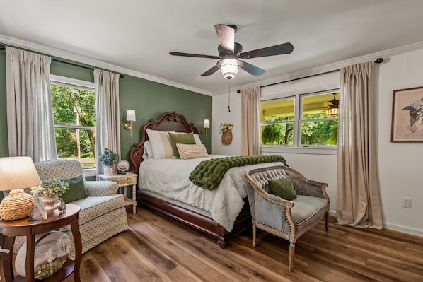A bedroom with a bed, a chair, a nightstand, a ceiling fan, and a window with curtains.