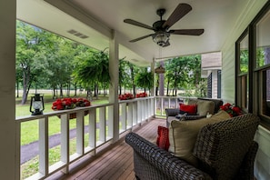 A covered porch with a ceiling fan, wicker furniture, and a view of a park.