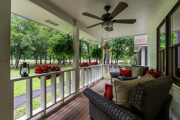 A covered porch with a ceiling fan, wicker furniture, and a view of a park.